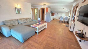 Ein Wohnzimmer mit Sofa, Couchtisch und Küchenzeile, inklusive Kühlschrank und Esstisch.