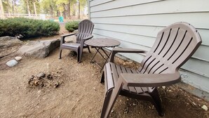 An outdoor seating area with two Adirondack chairs and a small table, positioned on a dirt ground with sparse vegetation and rocks. - Historic Firehouse - Spacious, Private & Clean (Kachina Village)