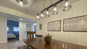 A spacious room with a long wooden table, a chair, and a potted plant. There are framed architectural drawings on the wall. - Historic Firehouse - Spacious, Private & Clean (Kachina Village)