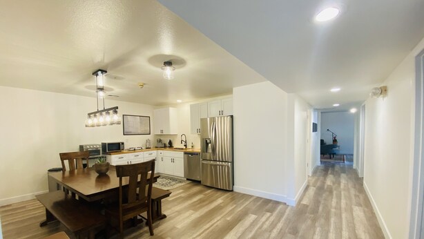A modern kitchen with white cabinets, stainless steel appliances, and a wooden dining table with chairs. - Historic Firehouse - Spacious, Private & Clean (Kachina Village)