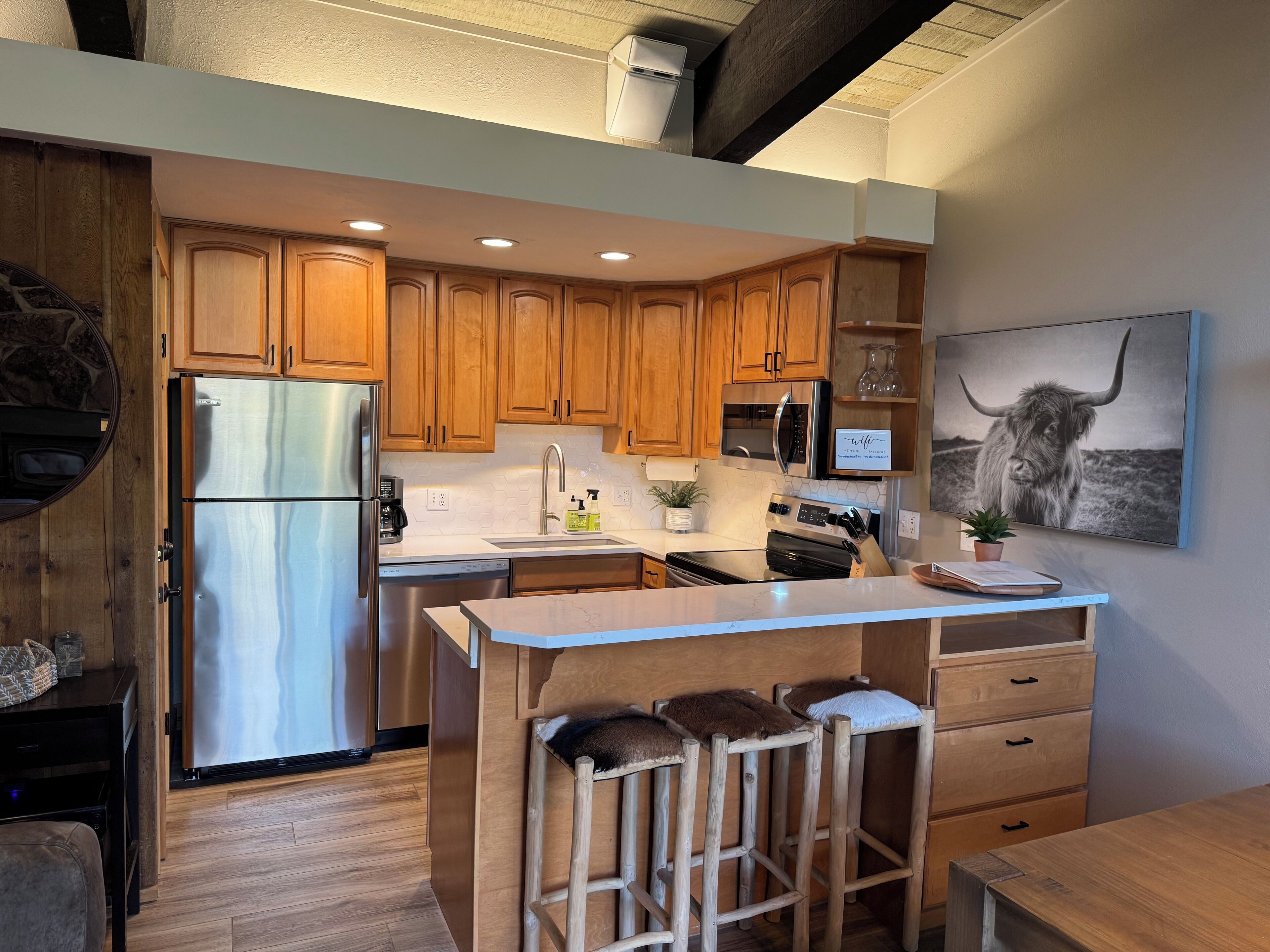 Una cocina moderna con armarios de madera, electrodomésticos de acero inoxidable y una zona de bar con taburetes.