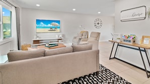 A modern living room with a sofa, a coffee table, a TV, and a desk with a plant and books. - Renovated Townhome near Oldtown Scottsdale (Large Patio and Community Pool) (Scottsdale)