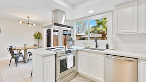 A modern kitchen with white cabinetry, a built-in oven, a dishwasher, and a window with a view of palm trees. - Renovated Townhome near Oldtown Scottsdale (Large Patio and Community Pool) (Scottsdale)