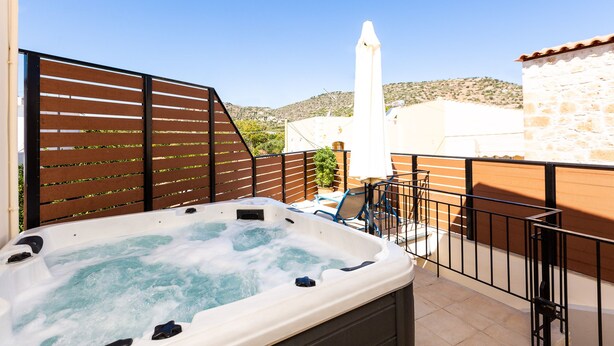 A hot tub in an outdoor patio area with a wooden fence, a stone wall, and a view of hills in the background. - Maria's Place, a great place to experience Crete! (Rethymno)