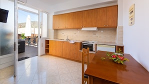 A modern kitchen with wooden cabinets, a built-in oven, and a dining area with a table and chairs. - Maria's Place, a great place to experience Crete! (Rethymno)