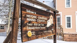 Señal de madera que da la bienvenida a visitantes a la región histórica minera de Colorado, con un casco de minero y un mensaje sobre la protección del patrimonio histórico de Colorado.