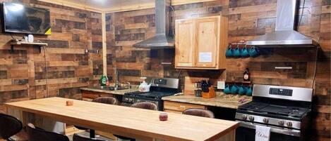 A kitchen with wooden walls, a wooden table, chairs, a stove, a microwave, and cabinets.