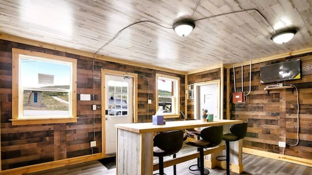 Una habitación con paredes de madera, una zona de bar y un televisor colgado en la pared.