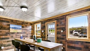 Una habitación con paneles de madera, una mesa larga con sillas, una ventana que da a un vehículo en el exterior y una puerta que conduce a otra habitación.