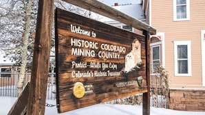 Señal de madera dando la bienvenida a visitantes al histórico territorio minero de Colorado, con un casco de minero y un mensaje sobre la protección de los tesoros históricos de Colorado.