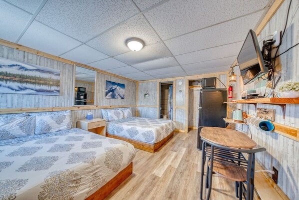 Ein kompaktes Zimmer mit zwei Betten, einer kleinen Küchenzeile, einem Fernseher und einer Kaffeestation.