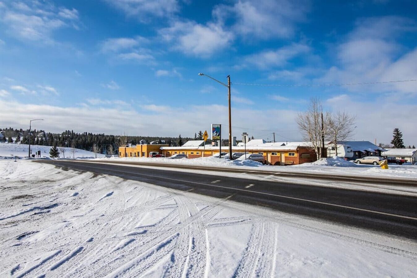 A snow-covered road with a motel and a gas station in the background.