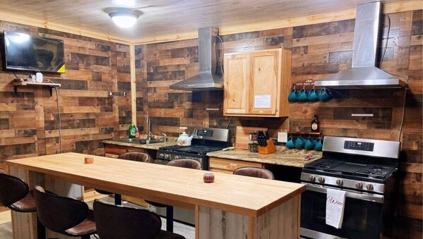 A kitchen with wooden walls, a wooden dining table, and two stoves.