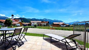 Une terrasse avec une table et des chaises, un chemin de gravier et, au fond, des maisons aux toits rouges.