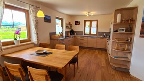 Une cuisine chaleureuse avec des meubles en bois, une table à manger et des chaises. Une fenêtre offre une vue sur un paysage verdoyant.