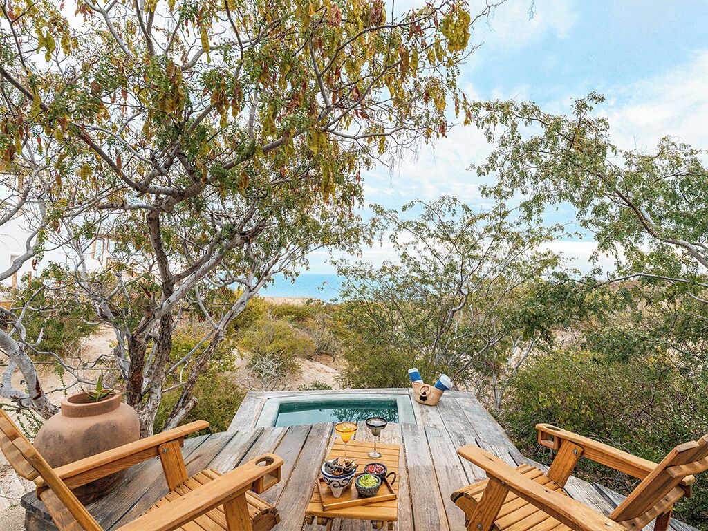 A wooden deck with a pool, surrounded by trees and a view of the ocean.