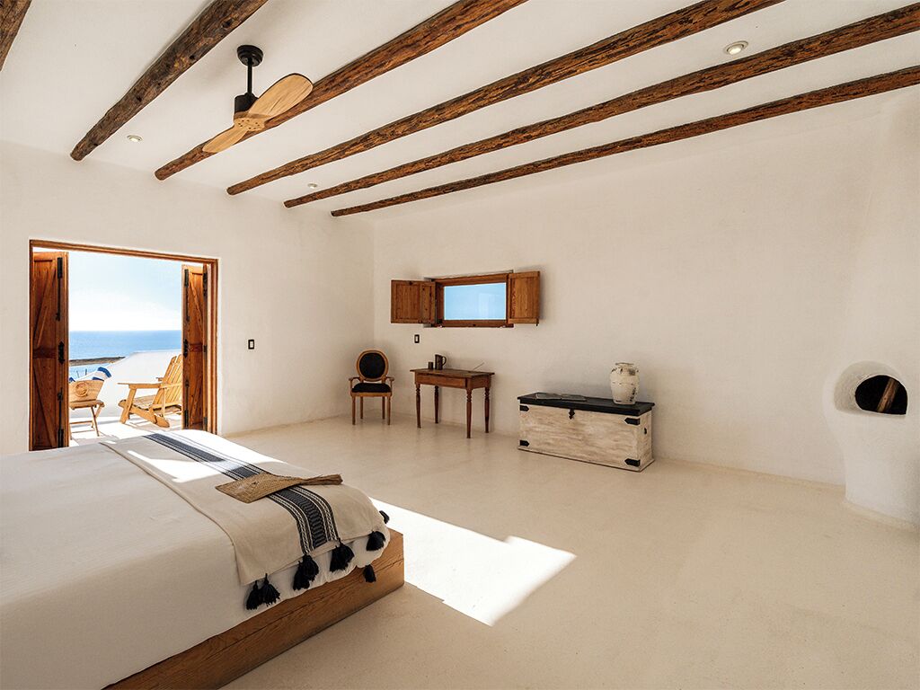 Un dormitorio con cama, vigas de madera, televisor, una mesita y vista al mar.