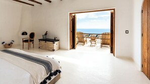 A bedroom with a large bed, wooden beams, a desk, and a view of the beach. - NEST Baja, Member of Design Hotels (La Fortuna)