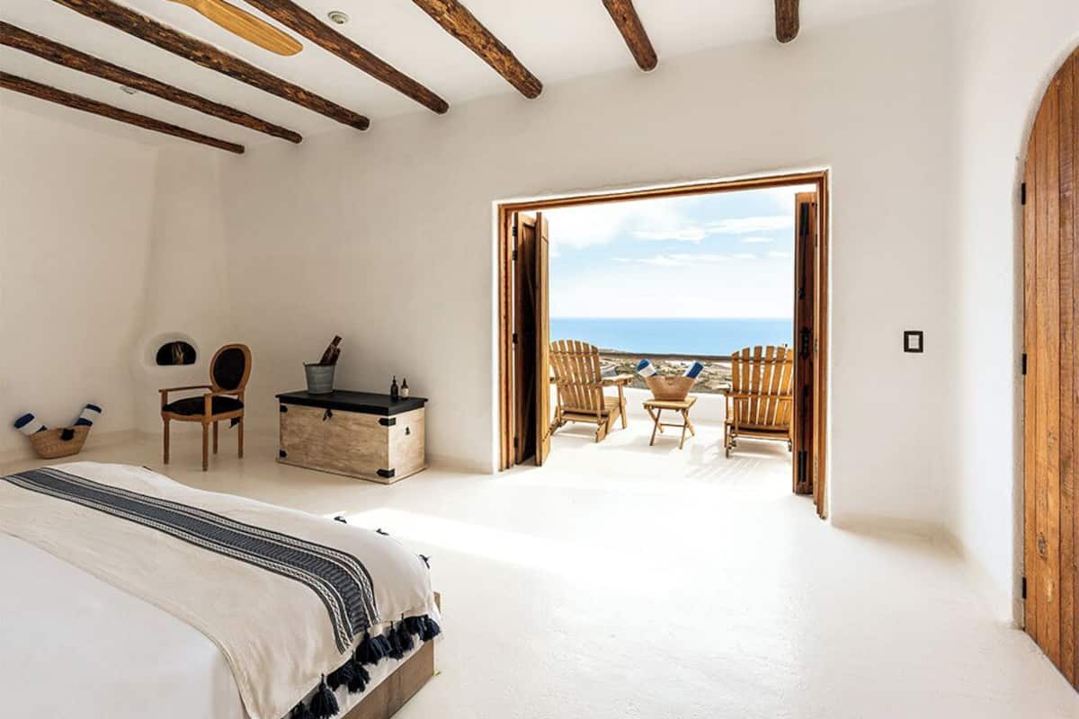 A bedroom with a large bed, wooden beams, a desk, and a view of the beach.