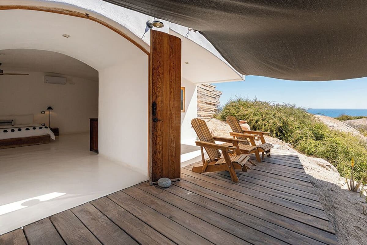 A modern beach house with a wooden deck, outdoor seating, and a view of the ocean.