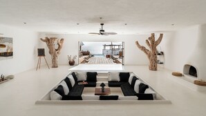 A modern living room with a central sectional sofa, a ceiling fan, and a view of an outdoor deck. - NEST Baja, Member of Design Hotels (La Fortuna)