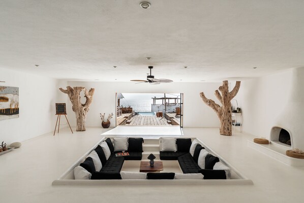 A modern living room with a central sectional sofa, a ceiling fan, and a view of an outdoor deck. - NEST Baja, Member of Design Hotels (La Fortuna)