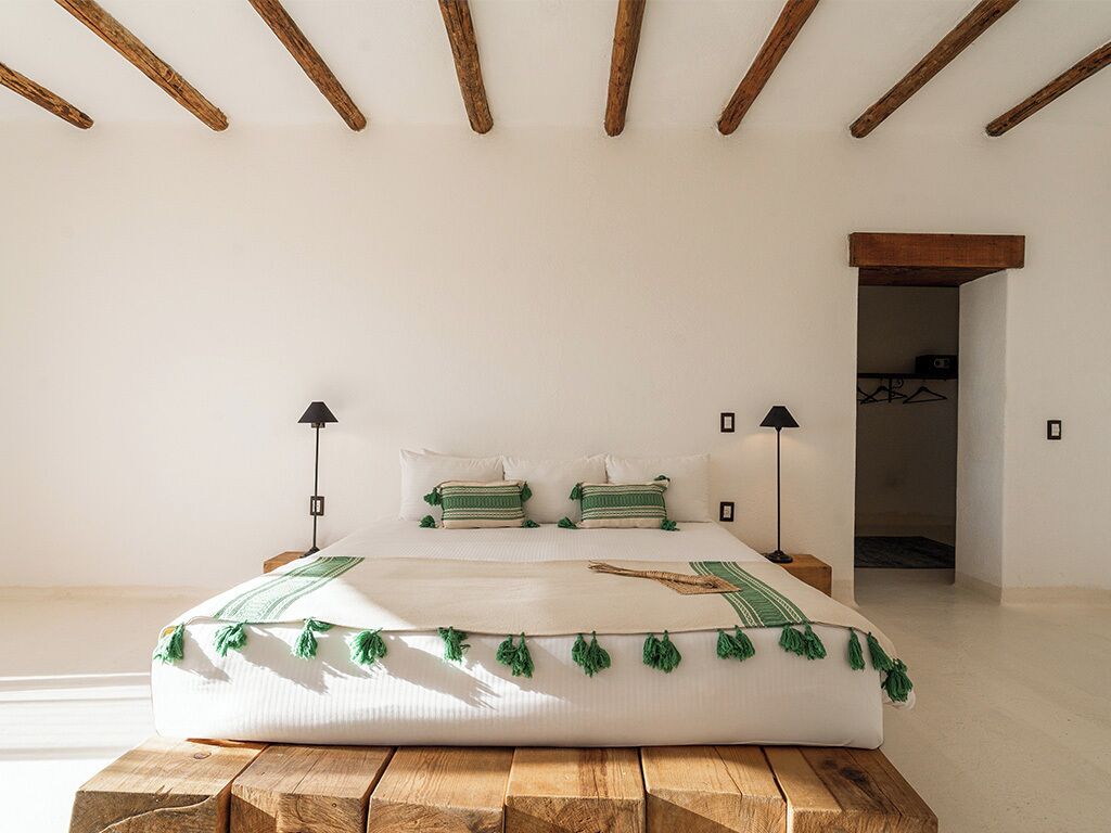 Un dormitorio con una cama grande, vigas de madera en el techo y una puerta que conduce a otra habitación.