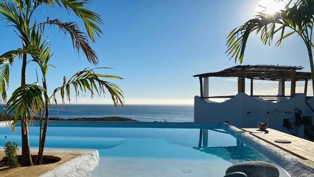 A clear view of a swimming pool with a view of the ocean, surrounded by palm trees and a wooden structure. - NEST Baja, Member of Design Hotels (La Fortuna)