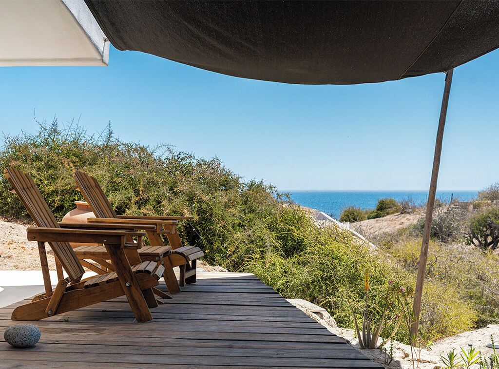 A wooden deck with lounge chairs and a table overlooking a coastal landscape.