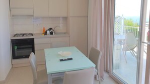 A compact kitchen with a gas stove, sink, and a small countertop. There is a dining table with chairs and a view of the outdoors through a glass door. - Appartamenti Borgo Panoramico N.9 (Tropea)