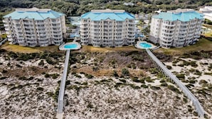 Un hôtel situé en bord de mer, composé de plusieurs bâtiments, doté d’une piscine centrale et d’une promenade qui mène à la plage.