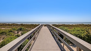 Une promenade en bois menant à une plage, avec un ciel dégagé.