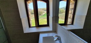 A bathroom with a bathtub, a window with a view of a green landscape, and a tiled wall. - Beautiful apartment in a Provencal farmhouse with swimming pool, ideal for family or friends (Viens)