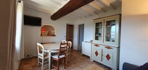 Un coin repas avec une table ronde et des chaises, un meuble avec des portes en verre et un téléviseur fixé au mur.