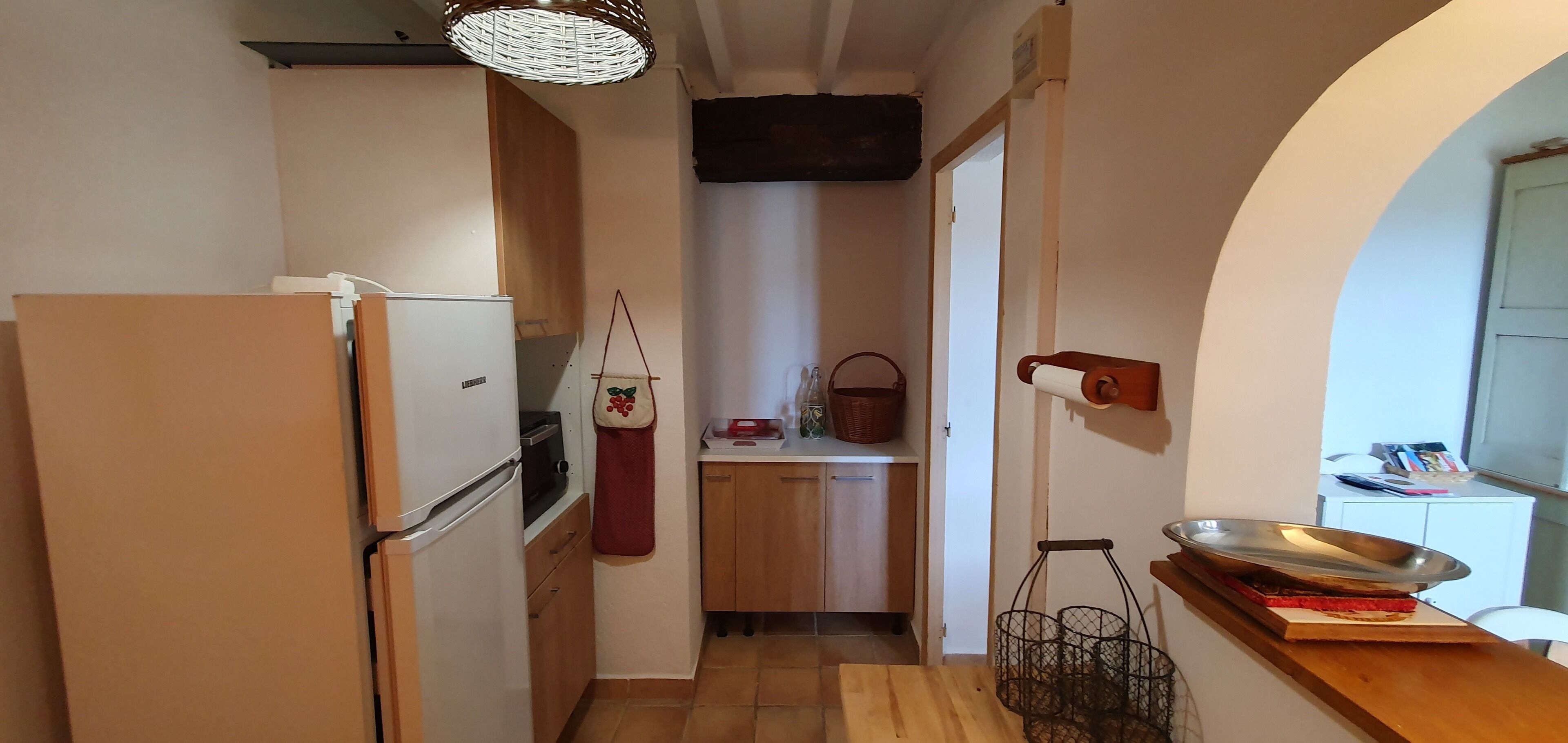 Une cuisine compacte comprenant un réfrigérateur, un meuble en bois, un panier suspendu et un plateau en métal posé sur le comptoir.
