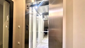 An elevator with a metallic finish, a control panel, and a glass door.