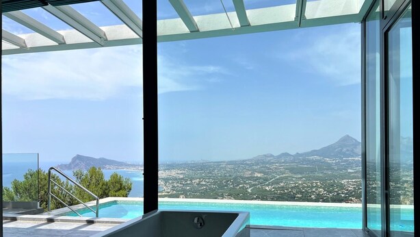 A modern bathroom with a large bathtub, a glass-enclosed shower area, and a view of a coastal landscape with mountains and a city in the distance.
