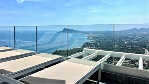A panoramic view from a high-rise balcony with clear skies, a coastal landscape, and a bridge in the distance.