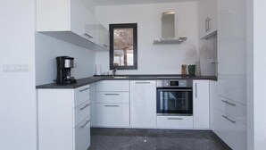 A modern kitchen with white cabinets, a black countertop, a built-in oven, and a coffee maker.