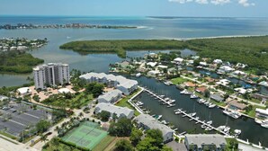 An aerial view of a coastal residential area with a marina, a tennis court, and a large building with multiple floors. - 18120 San Carlos Blvd PH2 (Fort Myers Beach)