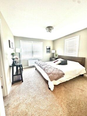 A bedroom with a bed, bedside tables, a lamp, a radiator, and a window with blinds.