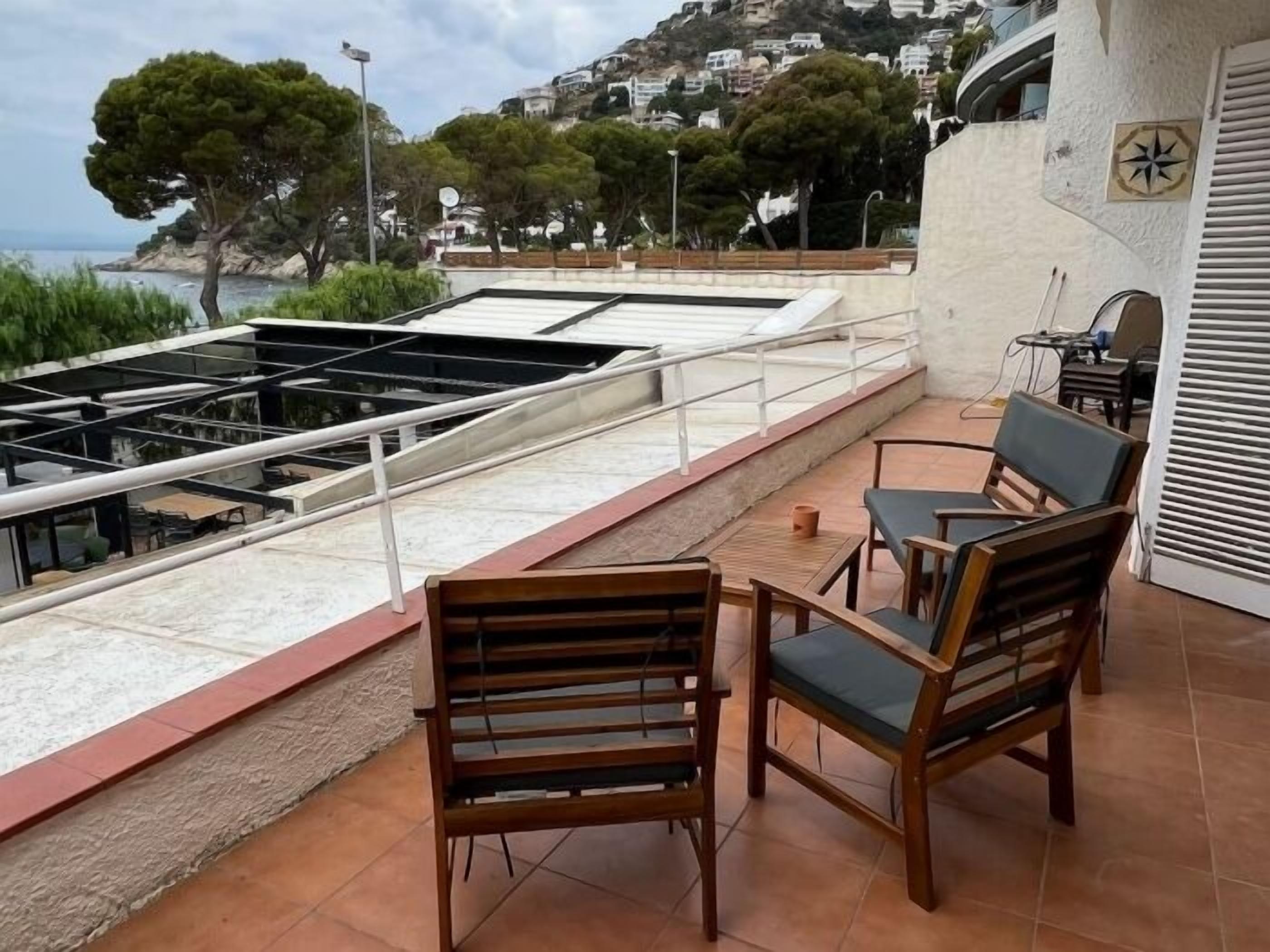 A terrace with a view of the sea, wooden chairs, and a table.