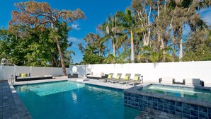 Une piscine entourée d’arbres et d’une clôture blanche, avec des chaises longues et un panier de basketball.