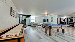 Un vaste espace de vie comprenant une table de billard, une table de baby-foot et un escalier menant à un niveau supérieur.