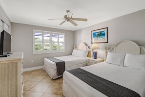 A hotel room with two beds, a ceiling fan, a TV on a dresser, and a window with blinds.
