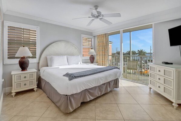 A bedroom with a bed, two bedside tables, a ceiling fan, a TV, and a balcony with a view.