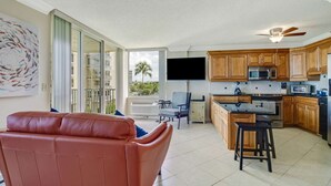 Un salón amplio con un sofá de cuero rojo, una cocina con armarios de madera y electrodomésticos modernos, y un balcón con vistas a palmeras.