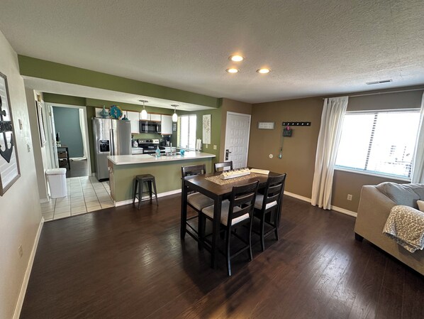 A modern kitchen with a central island, a dining area with a table and chairs, and a living room with a sofa.