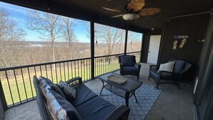 A covered balcony with wicker furniture, a ceiling fan, and a view of trees and buildings. - Lake Ozark Condo- Come stay & play! (Lake Ozark)