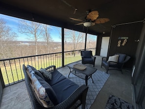 A covered patio with wicker furniture, a ceiling fan, and a view of trees and buildings.